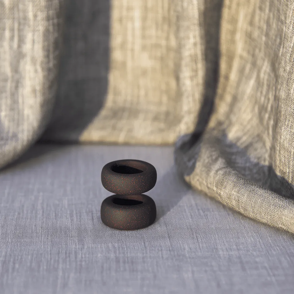 A black stacked object on grey linen beside a draped curtain.