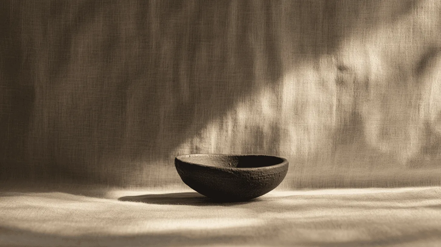 A dark ceramic bowl on creased linen in raking light.